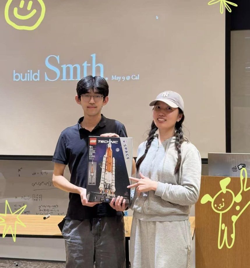 Two winners hold up a LEGO Technic space shuttle prize in front of the build Smth slide